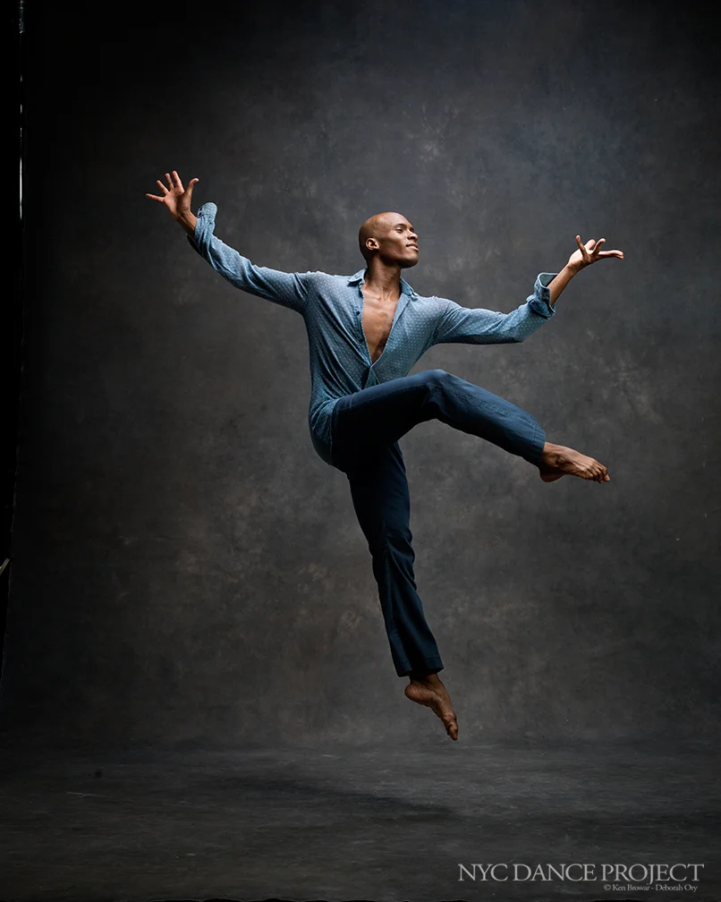 Jamal Callender dancing in a blue shirt, arms extended and one knee raised.